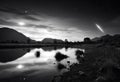 Monochrome sunset landscape with meteor in action. Starry sky with lake and hills at summer night