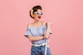 Enchanting pinup girl posing in sunglasses. Studio shot of slim young lady in striped blouse isolated on pink background