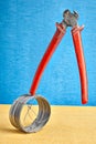 End cutter nipper teetering on steel wire coil, blue backdrop. Royalty Free Stock Photo