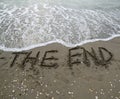 THE END text written on the sand and the wave that is erasing th Royalty Free Stock Photo