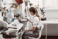 The End of the Working Day. Side view of young female jeweler sitting at her jewelry workshop and cleaning her workplace