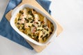 Endives or chicory gratin with apple, ham, cheese and pumpkin seeds in a casserole on kitchen board and a blue napkin, white table