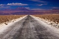 Endless dirt road with blurred mountain range in the horizon through salt flat