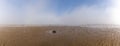 Endless ocean floor uncovered at low tide with sand structures and rocks and tidal pools under lifting fog in the blue sky Royalty Free Stock Photo