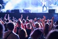 Energetic audience enjoys night concert, raising hands, recording live band on stage with smartphones. Festivalgoers