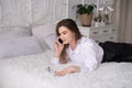 Energetic cute girl is lying on the bed with a phone