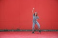 Energetic dancing teen girl cool moving raised fist outdoors on red wall background. Cool dancer perform hip hop dance