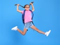 Energetic happy schoolgirl in eyewear with funny surprised facial expression jumping up in air