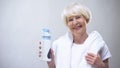 Energetic old woman with towel holding isotonic water, sport nutrition, health Royalty Free Stock Photo