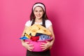 Energetic positive brunette housewife looks directly at camera, walking with pink basin with laundry, looks funny and happy.