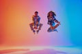 Energetic positive pair, dancers leaping in neon colorful illumination suspended in mid-air against gradient background.