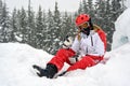 Energetic sporty woman in snowsuit sitting in the snow and showing an I like it or an I am happy with it signal