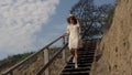 Energetic woman hurrying downstairs sand beach holding straw hat on head.