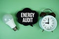 Energy Audit text with light bulb and alarm clock on green background Royalty Free Stock Photo