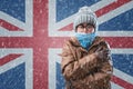 Energy crisis in Europe. Woman in hat, coat and scarf is warming herself. In the background is the flag of UK and a Royalty Free Stock Photo