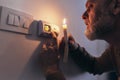 Man in complete darkness holding a candle to investigate thermostat during a power outage. Blackout concept Royalty Free Stock Photo