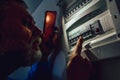 Man in complete darkness holding a phone to investigate a home fuse box during a power outage. Blackout concept