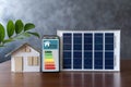 Energy efficiency mobile app on screen rating with arrows and house, text. Smart home display and model house with solar panel