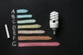 Energy efficiency rating chart, fluorescent light bulb and chalk on black background Royalty Free Stock Photo