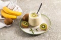 Energy fruit smoothie made of bananas and kiwi in a glass on a ceramic plate and a concrete background with fruit. the concept of