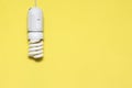 Energy saving lamp hanging from the ceiling, yellow background. Electricity conservation concept, place for text, copy space. The Royalty Free Stock Photo
