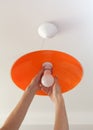 Energy-saving LED light bulb in the human hand, the replacement of the lamp in the ceiling luminaire made of orange ground glass. Royalty Free Stock Photo