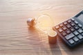 Energy saving light bulb with stacks of coins and calculator Royalty Free Stock Photo