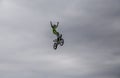 Aerial shot of stunt rider standing up in mid-air on his stunt bike against an overcast sky