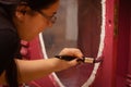 Engaged lady with brush in hand painting carved ornaments of antique cupboard door made of wood in pink color. Giving