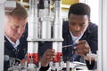 Engineer And Apprentice Working On Machine In Factory