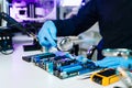 Engineer in blue gloves inspecting a computer motherboard with a magnifying glass in a tech lab. Concept of electronics repair, Royalty Free Stock Photo