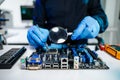 Engineer in blue gloves inspecting a computer motherboard with a magnifying glass in a tech lab. Concept of electronics repair, Royalty Free Stock Photo