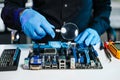 Engineer in blue gloves inspecting a computer motherboard with a magnifying glass in a tech lab. Concept of electronics repair, Royalty Free Stock Photo