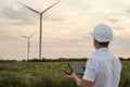 Engineer is checking energy production on wind turbine. Worker in windmills park in helmet and with tablet