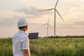 Engineer is checking energy production on wind turbine. Worker in windmills park in helmet and with tablet