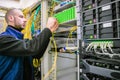 An engineer connects magistral optical fiber wires. A man commutes Internet wires in a server rack. The system administrator works