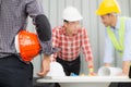 Engineer and construction team wearing safety helmet and looking blueprint on the table