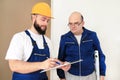 Engineer with his colleague, construction worker is measuring wall using spirit level tool, checking in apartment blueprint.