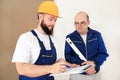 Engineer with his colleague, construction worker is measuring wall using spirit level tool, checking in apartment blueprint.