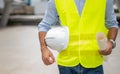 Engineer holding hardhat and floor plan wearing yellow vest and standing ready for work safety in site Royalty Free Stock Photo