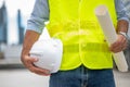 Engineer holding hardhat and floor plan wearing yellow vest and standing ready for work safety in site Royalty Free Stock Photo