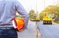 Engineer holding safety helmet at road construction site with roller compactor working asphalt road