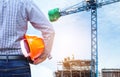 Engineer holding yellow safety helmet in building construction site with crane Royalty Free Stock Photo