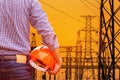 Engineer holding yellow safety helmet with high voltage electric pylon pillars in electric power plants substation on sunset Royalty Free Stock Photo