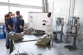 Engineer instructing apprentices at a whiteboard, side view