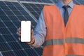 Engineer, man holding mobile phone, smartphone on a background of solar panels. White screen, place for image, text, application Royalty Free Stock Photo
