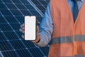 Engineer, man holding mobile phone, smartphone on a background of solar panels. White screen, place for image, text, application Royalty Free Stock Photo