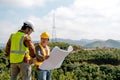 Engineer manager man discuss with his team who hold construction plan and stay in front of mountain view and  high voltage pole Royalty Free Stock Photo