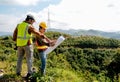 Engineer manager man discuss with his team who hold construction plan and stay in front of mountain view and  high voltage pole Royalty Free Stock Photo