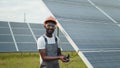 Engineer measuring amperage in solar panels outdoors. African man in grey overalls measuring resistance in solar panels